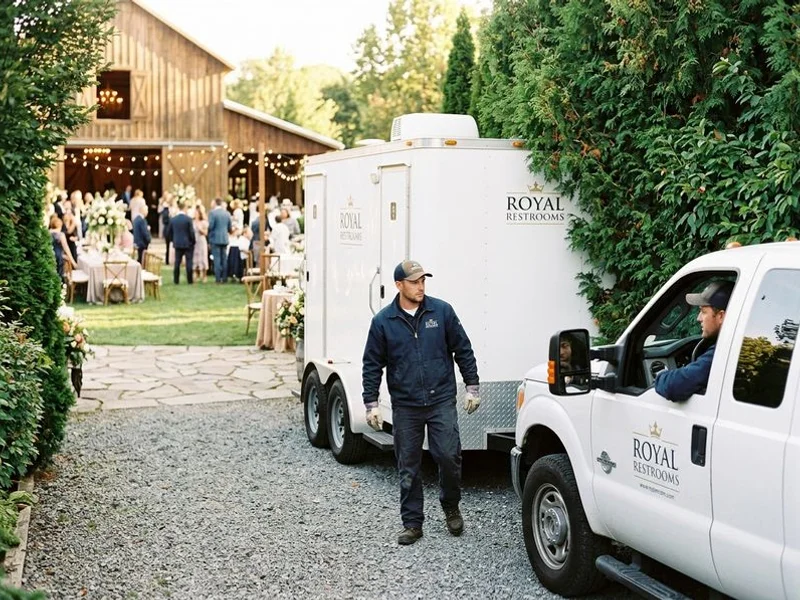 Restroom trailer placement screened by greenery at wedding venue